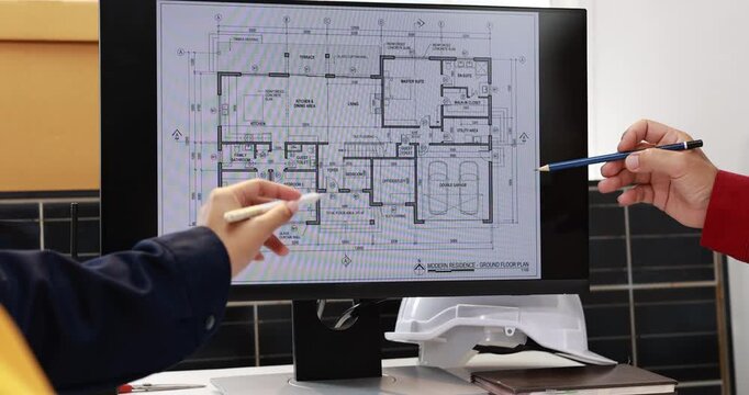 Architectural floor plan displayed on a computer monitor while a designer points with a pencil in a modern office.