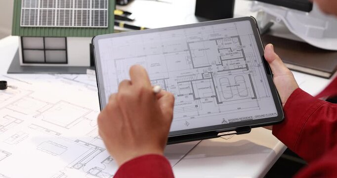 Architect reviewing a digital floor plan on a tablet while comparing printed building drawings at a desk.