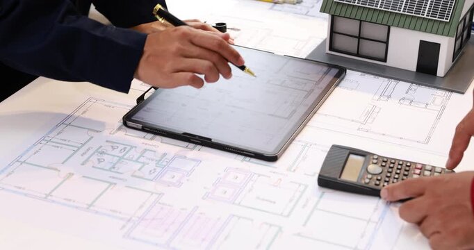 Architects reviewing building plans with a tablet, calculator, and scale model during an office design meeting