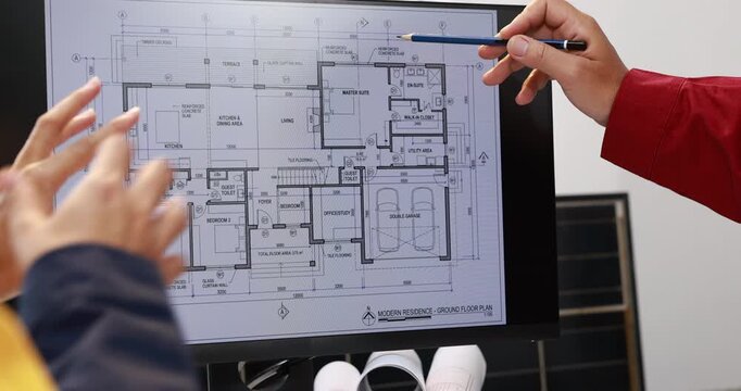 Architects discuss a residential floor plan on a computer screen, pointing and gesturing during a home design meeting in a modern office.
