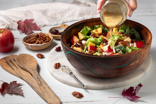 A hand pouring dressing onto a homemade Fall Harvest Salad
