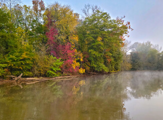 Vibrant autumn trees and morning mist reflecting on a calm lake. Ideal for seasonal nature designs, travel marketing, and wellness themes. © Julio
