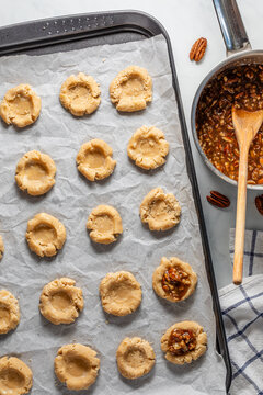 Rows of pecan cookies being filled with a caramel pecan mixture prior to baking.