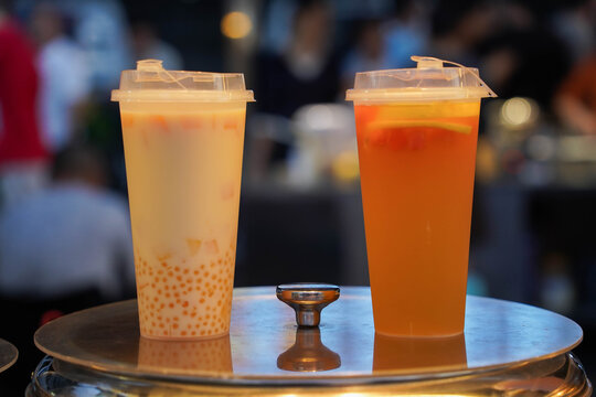 Two plastic cups of bubble tea, one white and one orange in night market