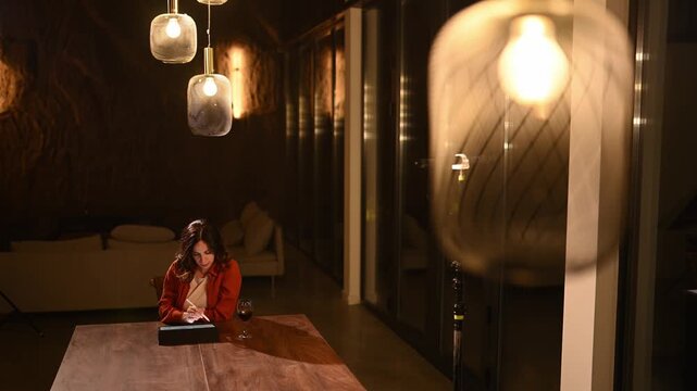 Woman freelancer finishing her remote work on a tablet at night, stretching while feeling satisfied in a modern apartment
