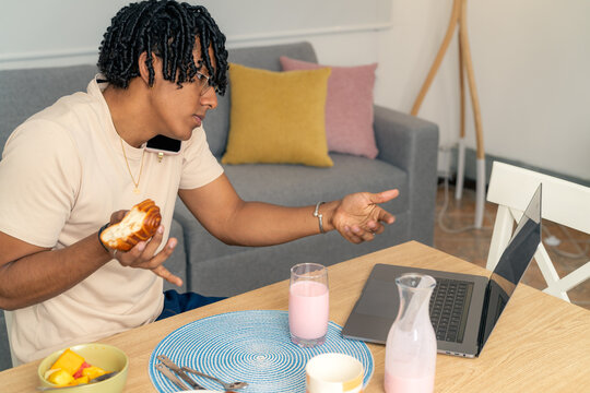 Young man multitasking working from home during breakfast