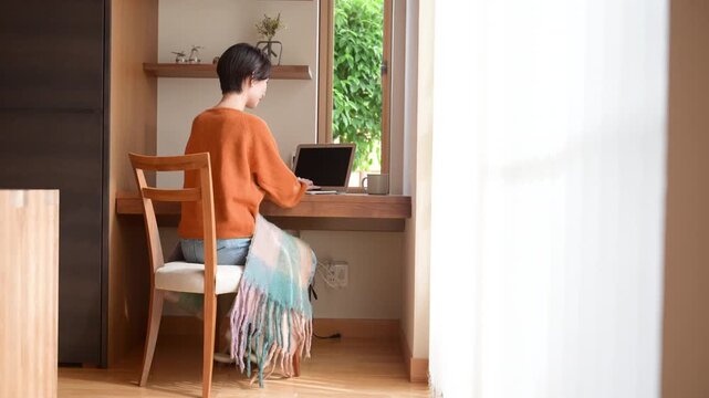 [秋冬]窓際にあるワークスペースで在宅ワークをする日本人女性、ノートパソコンを使う書斎のある家ライフスタイル顔なしの後姿全身動画