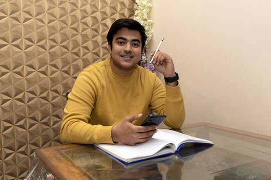 Portrait of happy Indian Male student study book at home Exams Preparations, Board Exams. 