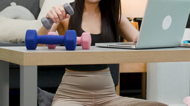 Asian Woman Exercising with Dumbbell While Working on Laptop at Home