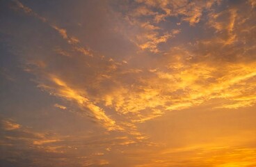 Soft golden clouds drift across the evening sky, illuminated by the warm glow of a stunning sunset. © Kirati