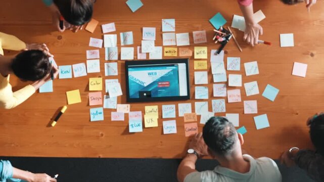Top down view of programmer brainstorming and planning about web design while looking at tablet wireframe prototype. Aerial view of skilled developer team talking about digital application. Symposium.