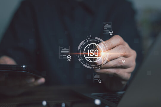 Manger hand touching glowing ISO standard certification hologram and digital compliance document over laptop. Concept of global quality control, corporate governance, and audit technology.