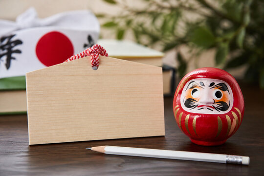 Blank ema votive plaque with a daruma doll and Japanese headband for exam success