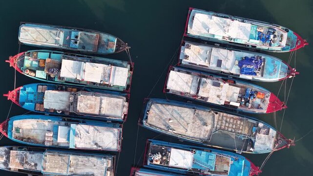 Aerial view of docked fishing boats in calm harbor water. Boats vary in size, color at Probolinggo