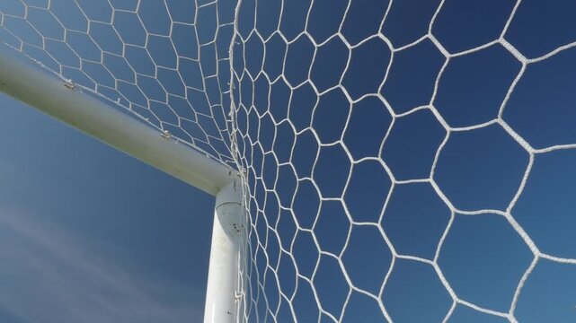 White synthetic football goal net with a hexagonal mesh pattern stands out against the azure sky.