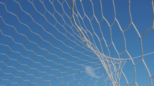 White synthetic football goal net with a hexagonal mesh pattern stands out against the azure sky.