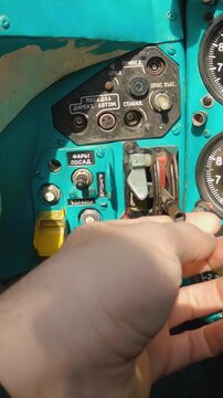 Hand operates switch on aged Mi-24 helicopter cockpit panel, gauges show pressure readings. Close up of helicopter cockpit control panel with analog dials, toggle switches, and Cyrillic labels