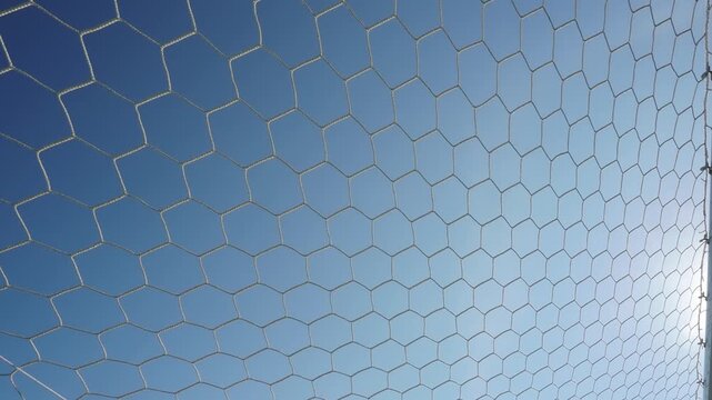 White synthetic football goal net with a hexagonal mesh pattern stands out against the azure sky.