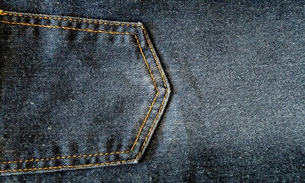 Close-up photo of a dark blue denim jeans pocket, showing the textured fabric, orange stitching detail, and slightly faded wash, casual style and fashion concept.