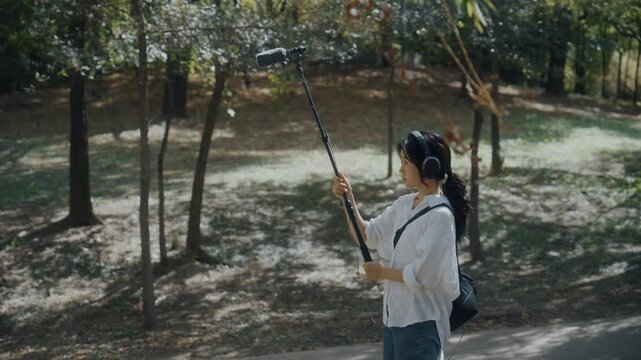 Young Asian Woman Wearing Headphones Listening to Nature Sounds in Park
