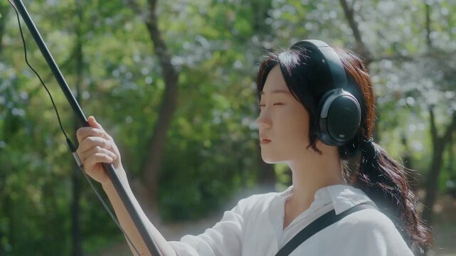 Young Asian Woman Wearing Headphones Listening to Nature Sounds in Park
