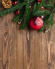 Festive Christmas background with red Ho Ho Ho ornament, evergreen fir branches, golden pinecone and decorative baubles on rustic wooden planks. Vertical holiday copy space for Christmas greetings © hannamartysheva