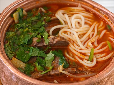Yunnan copper pot rice noodle with beef slices, cilantro, and bean sprouts in spicy red broth.