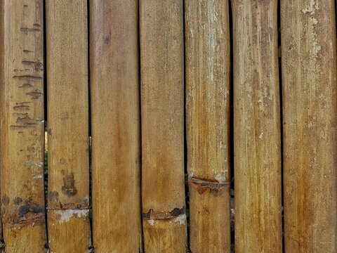 A close-up background texture of vertically aligned, weathered brown bamboo poles showing natural aged details, cracks, and rustic wooden patterns.