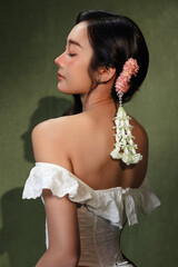 Side profile portrait of a beautiful young Asian woman wearing Malai an elegant Thai flower garland in her hair on a dark green background. © RedcupStudio