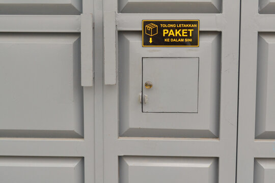 A sign for package drop-off on an iron door, in Indonesian, emergency exit door