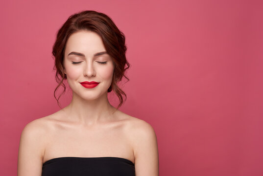 Young woman with red lipstick smiling against pink background