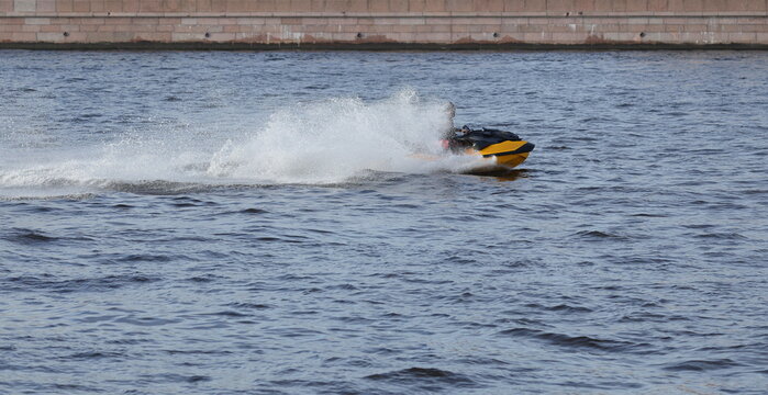 A yellow jet ski is speeding along the river at high speed, spraying water, alongside the granite embankment