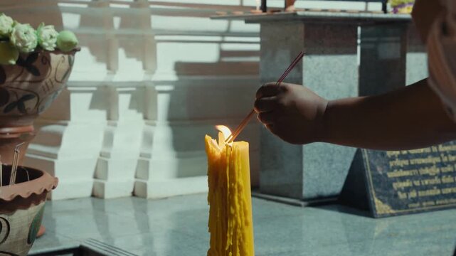 Worshippers ignite joss sticks at a melting wax taper by an altar, Thailand