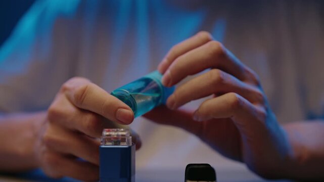 Man hands refilling vaporizer pod with flavored nicotine e liquid from bottle, routine maintenance procedure for reusable vaping system in dark room. Process of maintaining heated ecigarette.