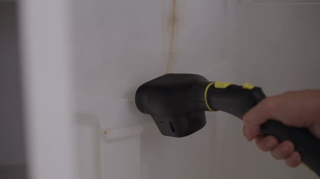 Professional cleaning service worker using powerful steam generator to disinfect and wash interior of dirty refrigerator, effectively removing grime and sanitizing surface, close-up, slow motion.