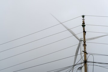 Utility pole and cables crossing a distant wind turbine © IbragimovN