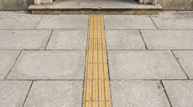 High Angle View of Yellow Tactile Paving Slabs for Blind and Visually Impaired People on Urban Concrete Sidewalk. Pathway Assistance for Disability Safety and Accessibility in Public Spaces.