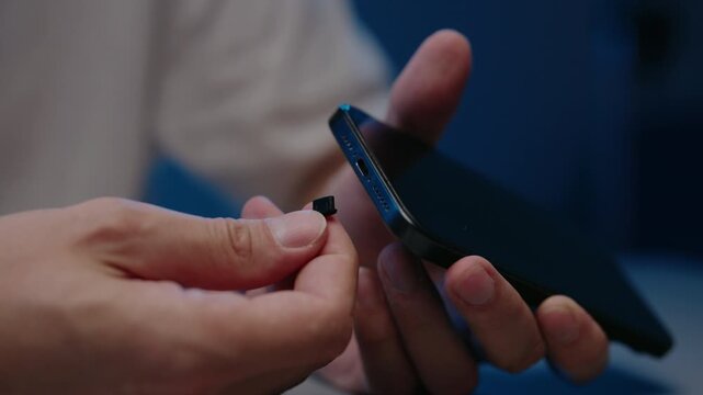 Hands inserting small black dust plug into charging port of cellular phone, protecting delicate connector from dirt, lint, moisture for reliable operation, close-up, slow motion.