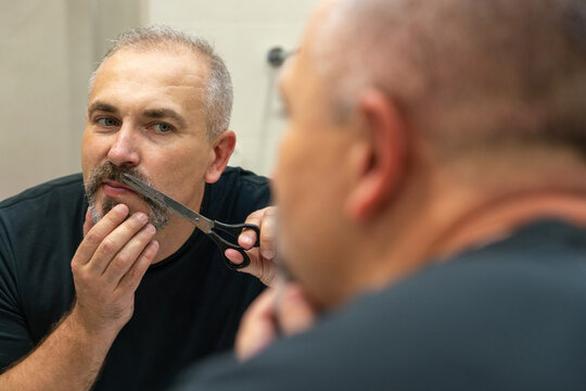 Portrait of Middle-aged handsome man cutting his beard and mooustache with scissors