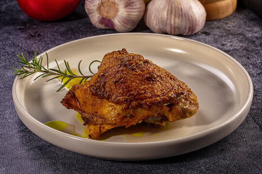 Crispy roasted chicken thigh with rosemary garnish and olive oil on a plate