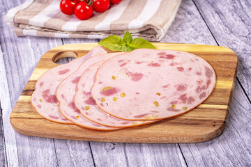 Slices of mortadella with olives and pink ham pieces on wooden cutting board with basil, cherry tomatoes and striped towel, deli meat food © Andrei Starostin