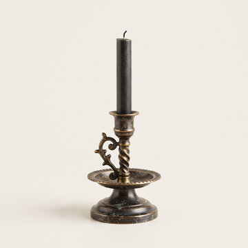 Antique brass candlestick with black candle on cream background