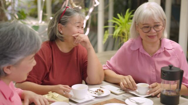 Senior woman rests hand beside white cup while listening to friends at leafy outdoor cafe, celebrating friendship, quality time, social connection through retirement lifestyle outdoors.
