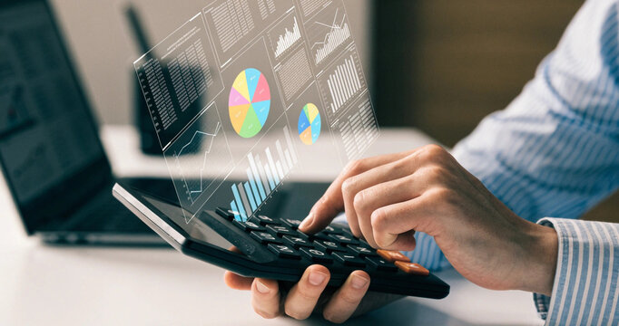 Business analyst using electronic calculator with holographic financial pie chart overlay display. Accountant calculating corporate budget metrics and data statistics using digital screen interface