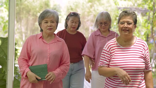 Four elderly friends walk together through leafy cafe garden while sharing relaxed conversation while sharing happiness, positive emotion, companionship through healthy aging lifestyle.