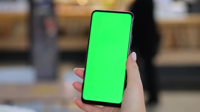 Hand holds phone with green screen. Background blurred in indoor setting. Three keyframes show same scene. Hand appears steady in each frame