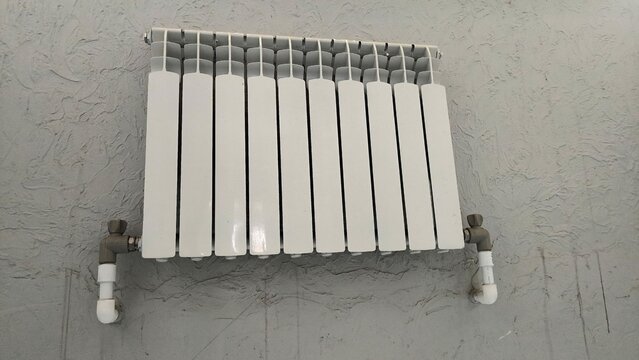 Modern white heating radiator mounted on textured grey wall inside room.