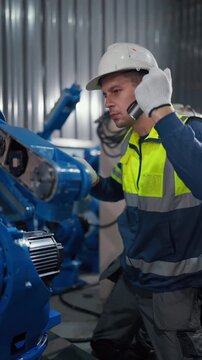 Worker adjusts machine with care and focus. He wears safety gear, helmet, gloves, and vest. Blue industrial equipment surrounds him