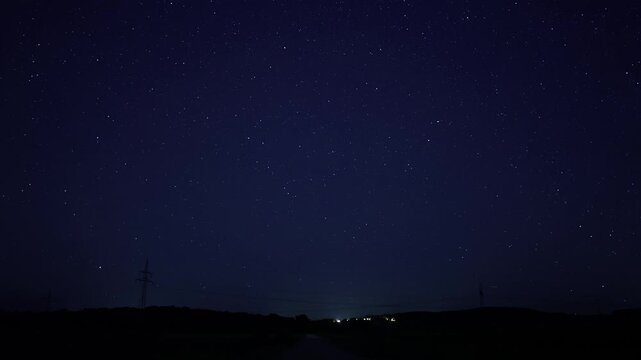 Time-Lapse of a field on a Perseid night, featuring the Milky Way, shooting stars, and a power supply in the background (Germany)