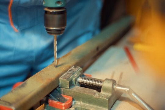 Close-up of a hand using a hand drill to bore a hole into a metal piece clamped in a vise. Authentic metalworking photo for industrial, construction and maker projects